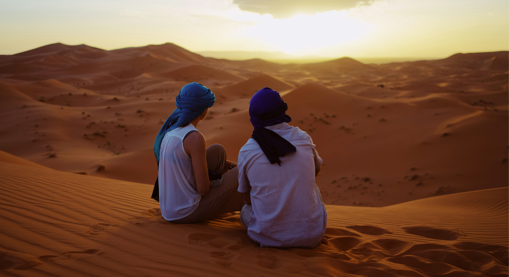 Two travelers sitting on a desert dune, a view from an authentic Foum Zguid desert adventure.